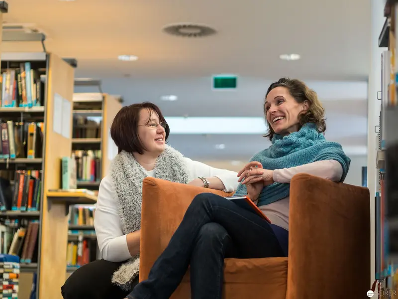 Two Women Sharing a Moment of Laughter in a Library Reading Area