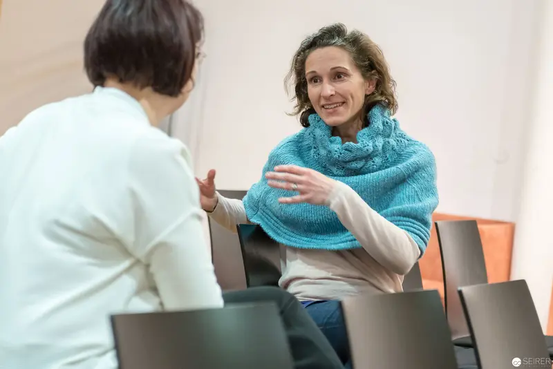 Two Women in Conversation, Seated in Neutral Interior Setting
