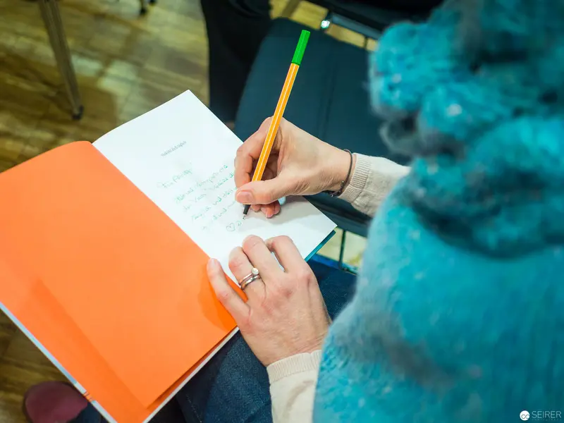 Close-Up of Hand Writing in Orange and White Notebook with Pencil