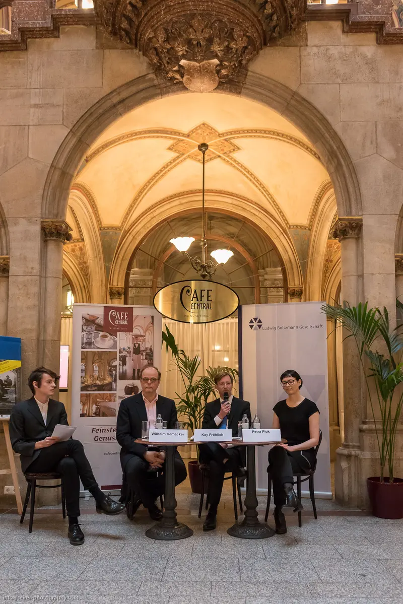 Panel Discussion at Ornate Café with Seated Participants Under Architectural Arch