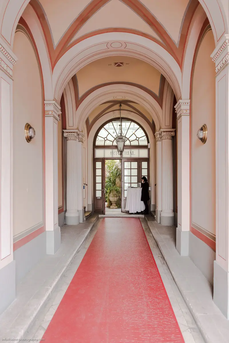 Elegant Arched Hallway with Red Carpet Leading to Sunlit Doorway