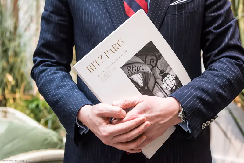 Elegantly Attired Individual Holding Ritz Paris Magazine in Pinstripe Suit