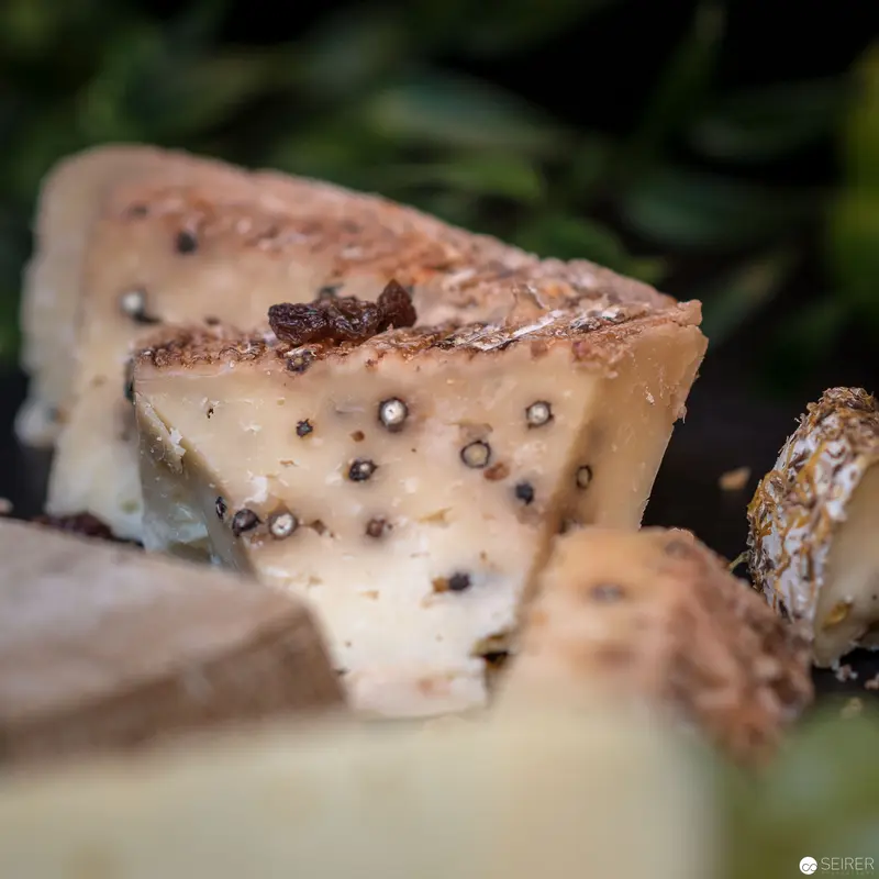 Textured Artisan Cheese Wedge with Black Pepper Inclusions against Verdant Background