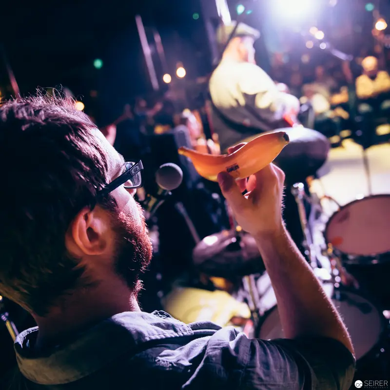 Musician Gesturing with Paper Airplane at Dimly Lit Concert Performance