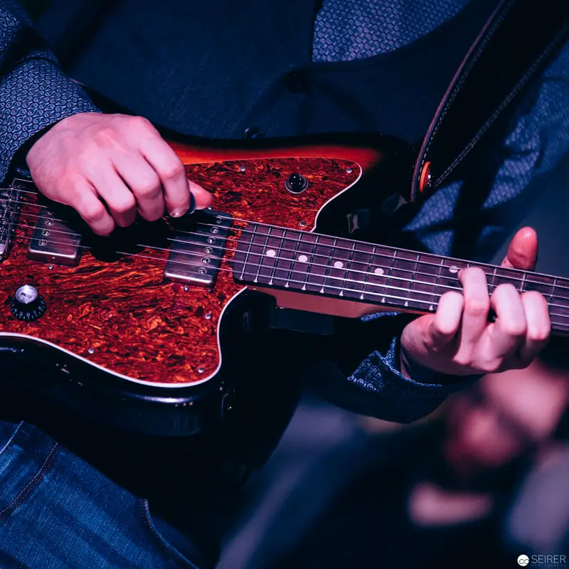 Electric Guitar Performance with Vibrant Red Tortoiseshell Pickguard in Low Light