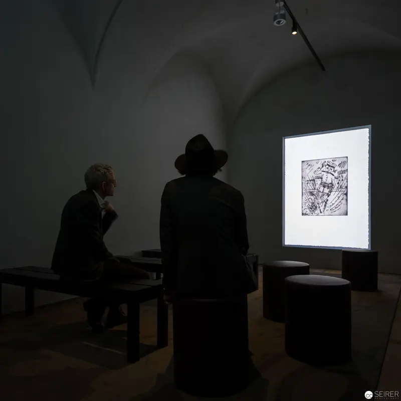 Two Silhouettes Contemplating Artwork in Dimly Illuminated Gallery Space