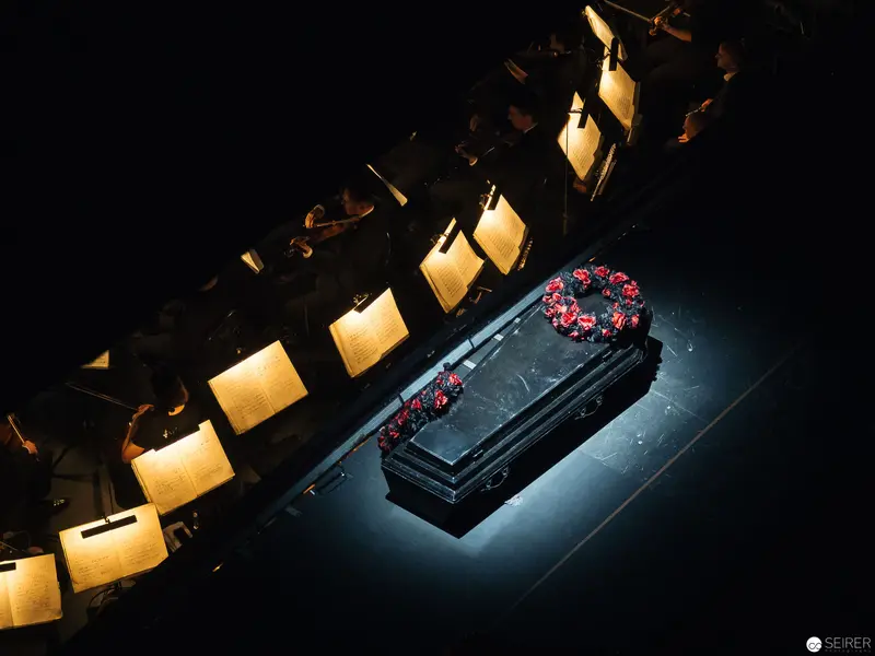 Dramatic Staging of Funeral Scene with Illuminated Backdrop in Theatrical Production