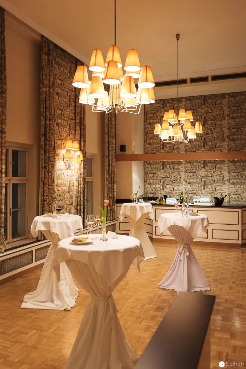 Elegant Event Space with White-Draped Tables and Chandeliers in Warm Illumination