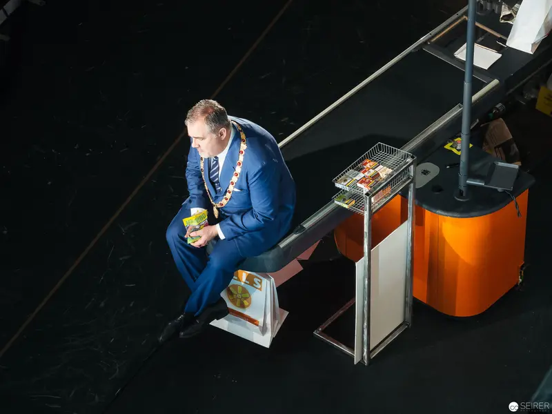 Municipal Official in Blue Suit Seated at Technical Workstation During Performance
