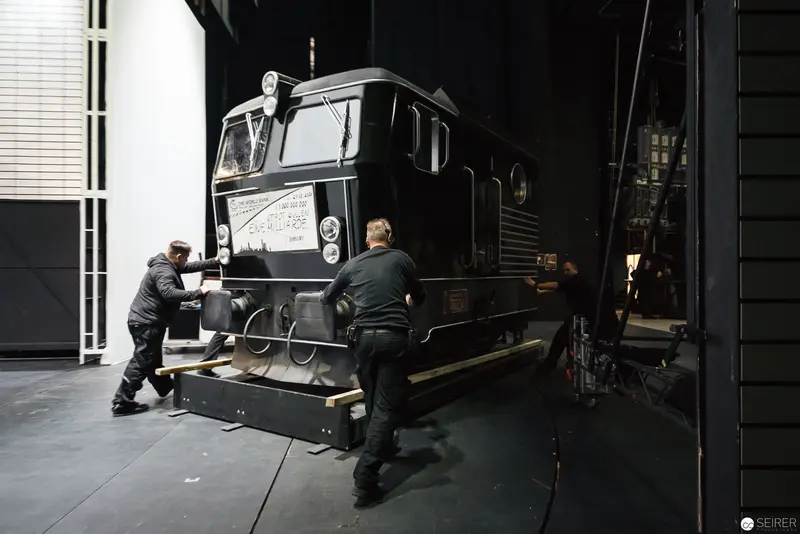 Industrial Staging Crew Preparing Locomotive Set Piece in Dark Theater Workshop