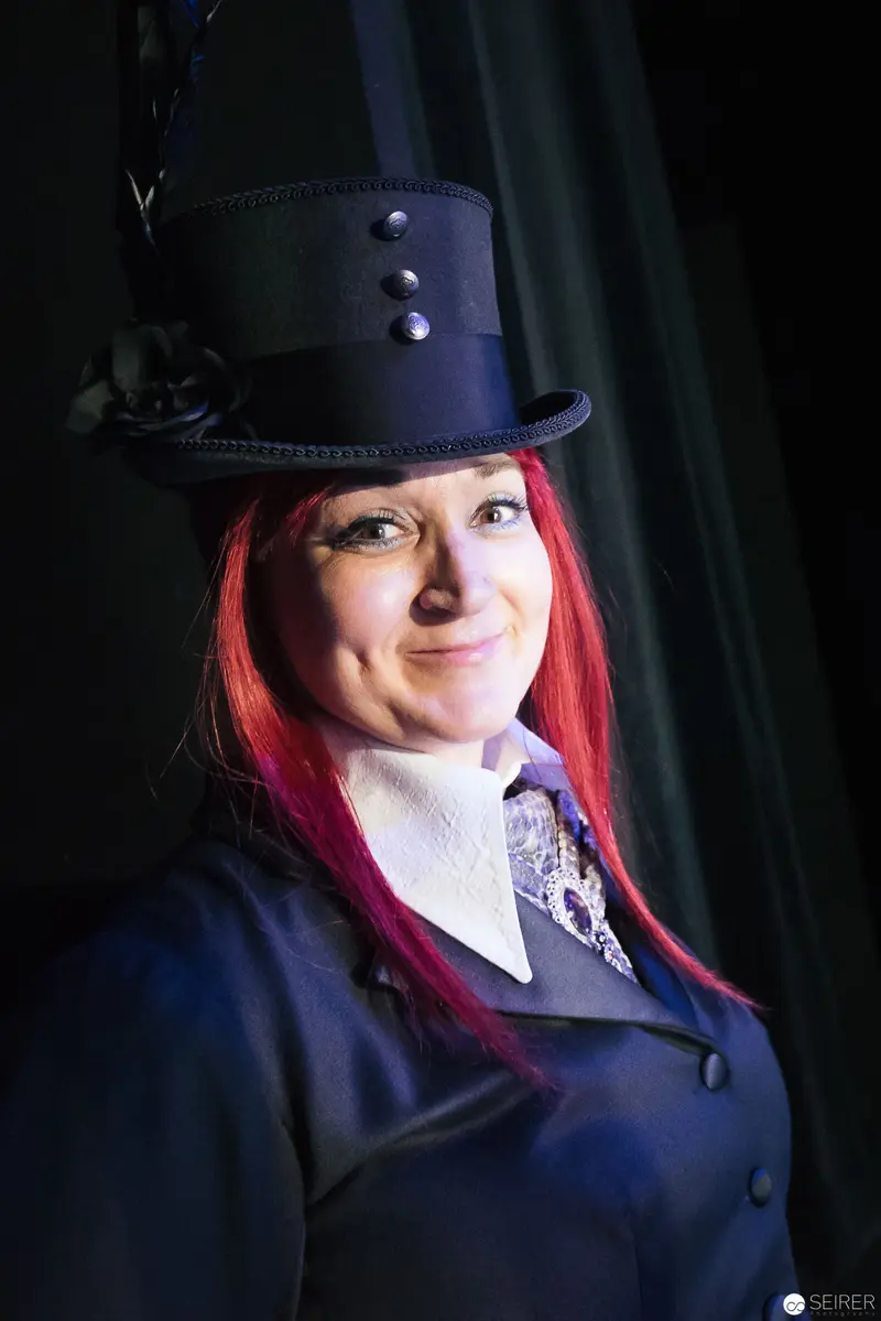 Theatrical Portrait in Top Hat with Vibrant Red Hair against Dark Backdrop