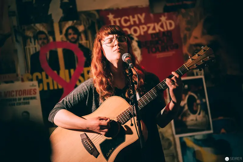 Singer-Songwriter Performs Acoustic Set at Indie Music Venue with Vintage Posters
