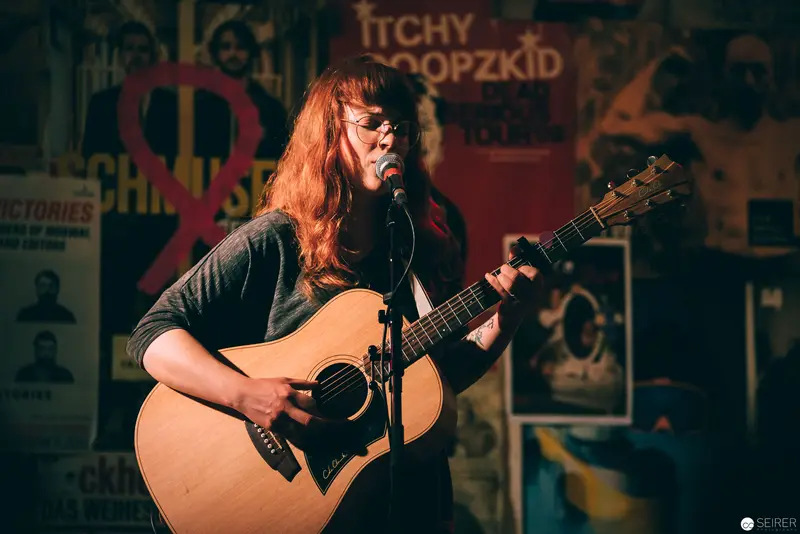 Acoustic Performer on Stage with Vintage Music Posters Background