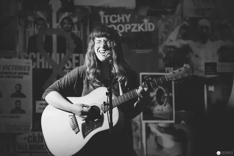 Acoustic Performer Laughing Mid-Song Against Vintage Poster Backdrop