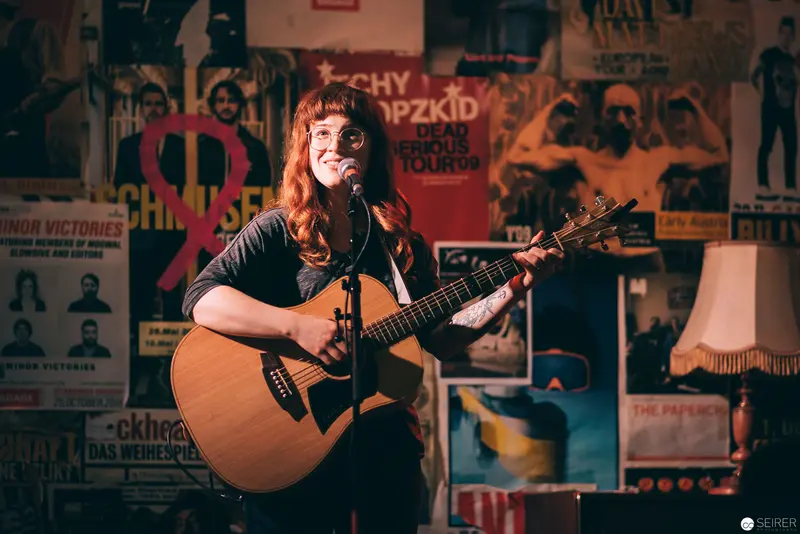 Singer-Songwriter Performing Solo Acoustic Set Against Vintage Music Poster Wall