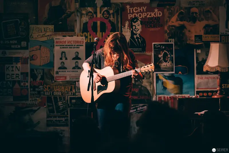 Acoustic Performance in Vintage Poster-Lined Venue with Ambient Stage Lighting