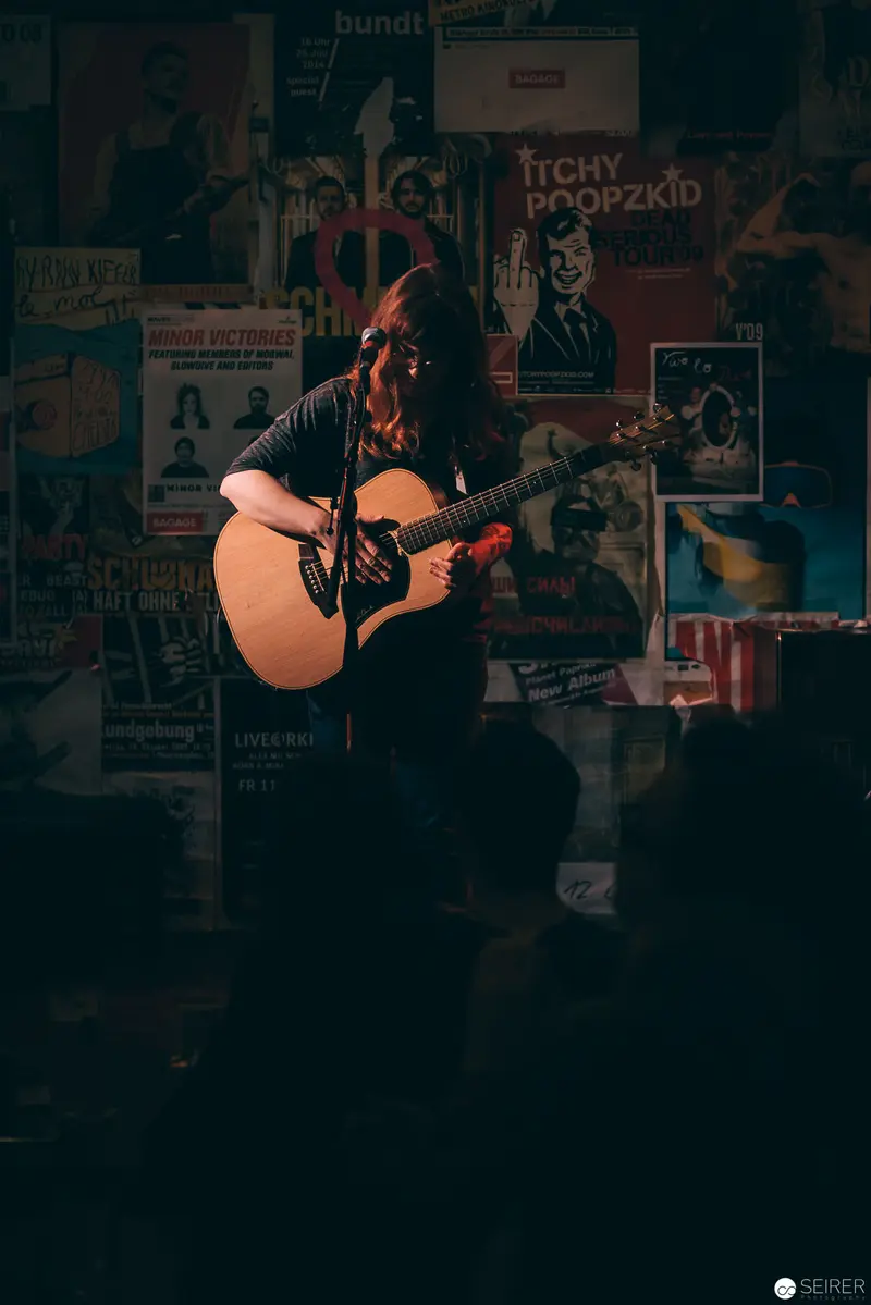 Acoustic Performer Silhouetted Against Vintage Music Posters in Dimly Lit Venue
