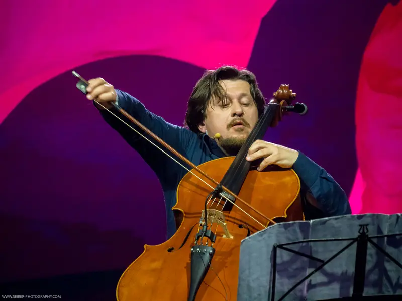 Intense Cellist Performing at 4GameChangers Festival with Dramatic Backdrop