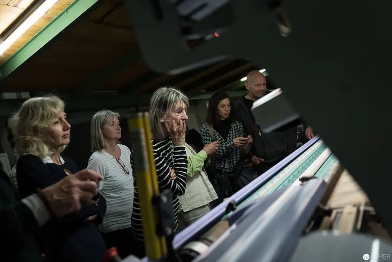 Women Observing Industrial Printing Equipment in Dimly Lit Workshop Space