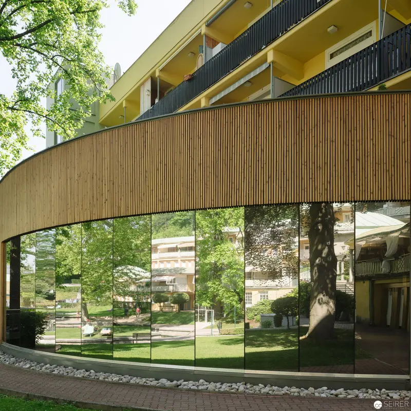 Curved Glass Facade Reflecting Verdant Landscape at Thermalbad Bad Vöslau