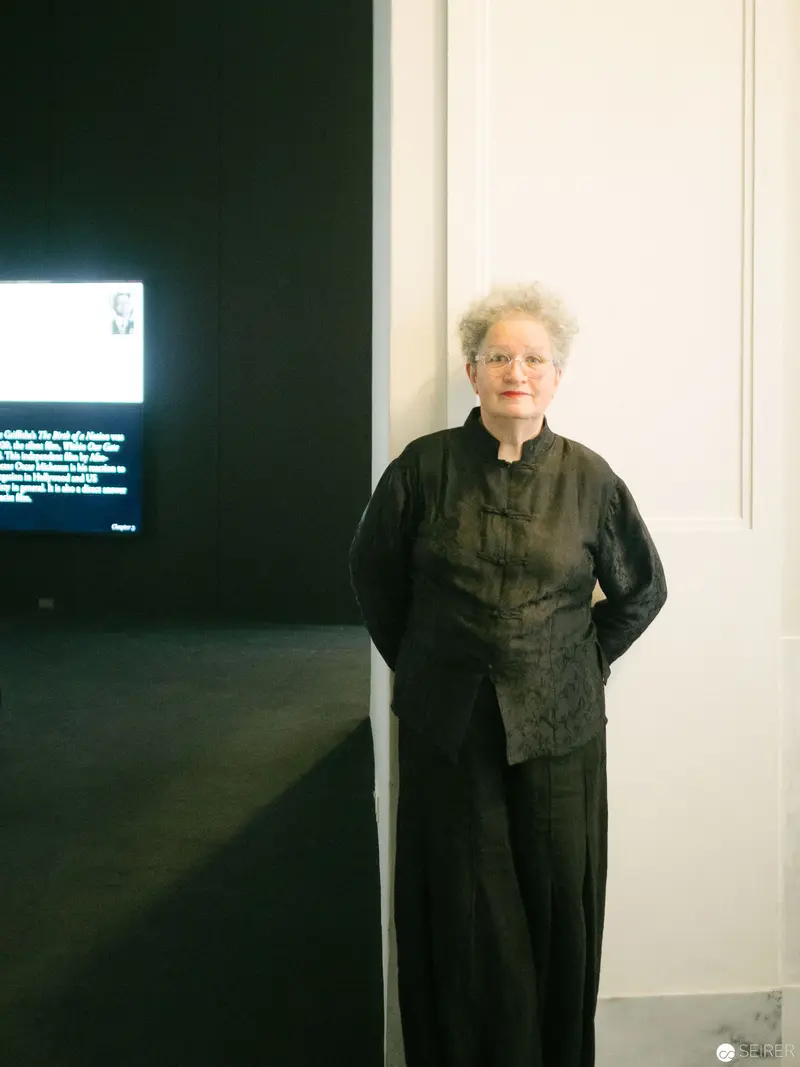 Elderly Person Standing in Minimalist Gallery Space with Dark Background