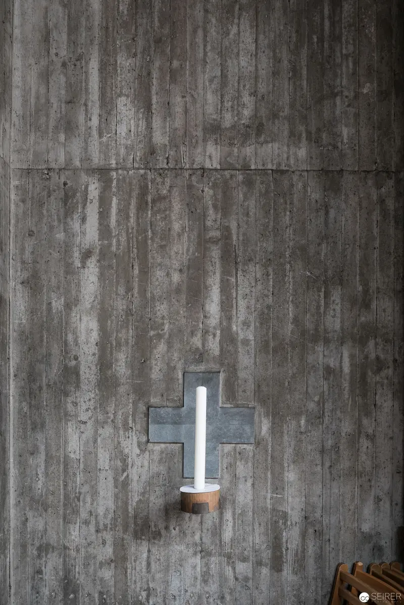 Minimalist Cross Light Fixture Against Weathered Concrete Wall at Pfarre Oberbaumgarten