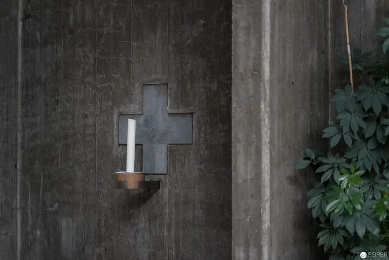 Cross-Shaped Memorial Lamp on Textured Concrete Wall at Oberbaumgarten Parish