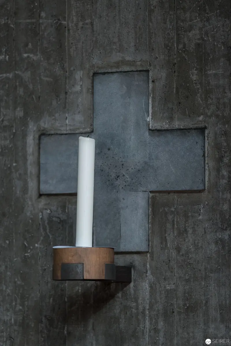 Minimalist Cross and Candle on Textured Concrete Wall at Pfarre Oberbaumgarten