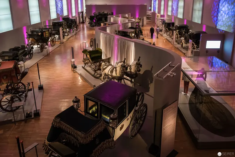 Historic Carriages Exhibition with Dramatic Purple Lighting and Ornate Horse-Drawn Vehicles