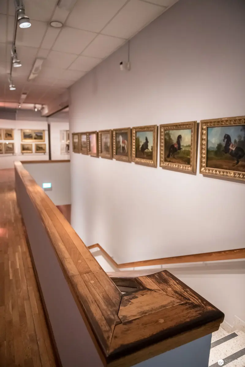 Gallery Interior with Framed Landscape Paintings and Wooden Staircase