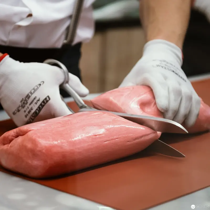 Precise Butchery: Skilled Hand Slicing Raw Pink Meat with Professional Knife