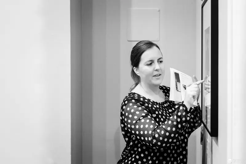 Woman in Polka Dot Dress Examining Framed Artwork on Wall