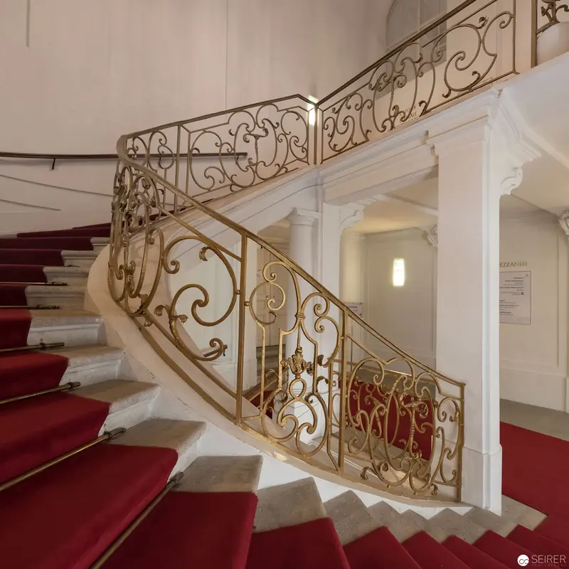 Ornate White Marble Staircase with Gilded Wrought-Iron Railing and Red Carpet