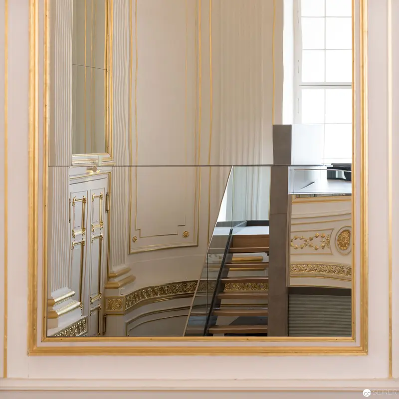 Ornate Interior Reflected: Neoclassical Wall and Staircase through Gilded Mirror Frame