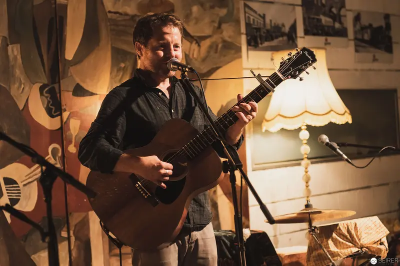 Acoustic Performer in Intimate Venue with Vintage Lamp and Wall Decor