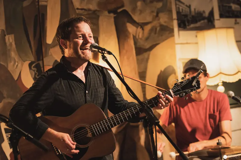 Intimate Acoustic Performance with Guitarist and Drummer in Warm-Lit Venue