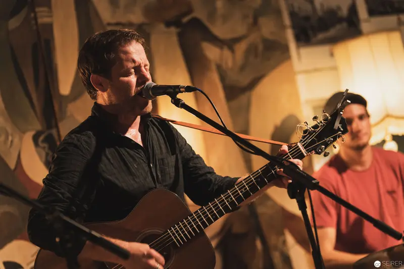 Acoustic Guitarist Performing Intimate Concert with Microphone and Companion