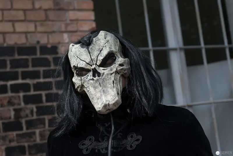 Haunting Skull Mask with Black Hair Against Brick Wall Backdrop