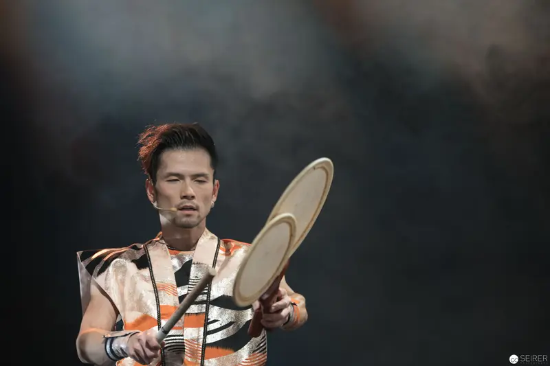 Takuya Taniguchi Performing Percussive Rhythms in Energetic Orange Stage Costume