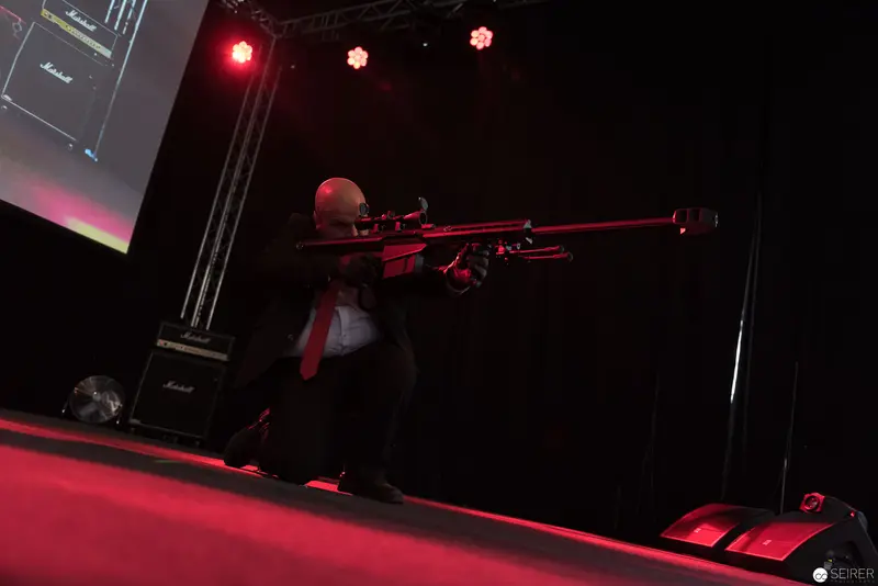 Performer with Long Rifle on Dimly Lit Stage with Red Lighting