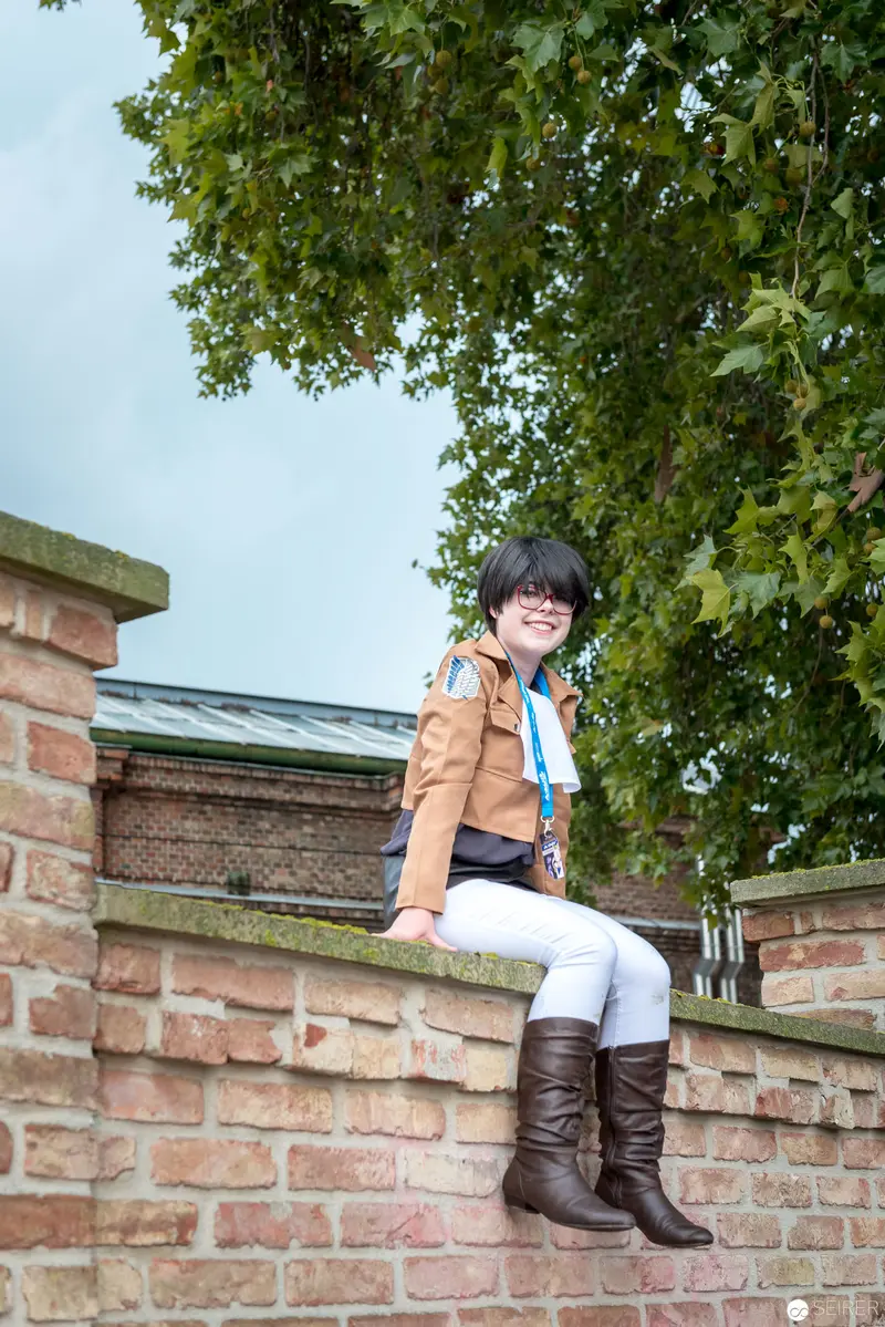 Young Person in Autumn Attire Seated on Brick Wall Near Verdant Foliage