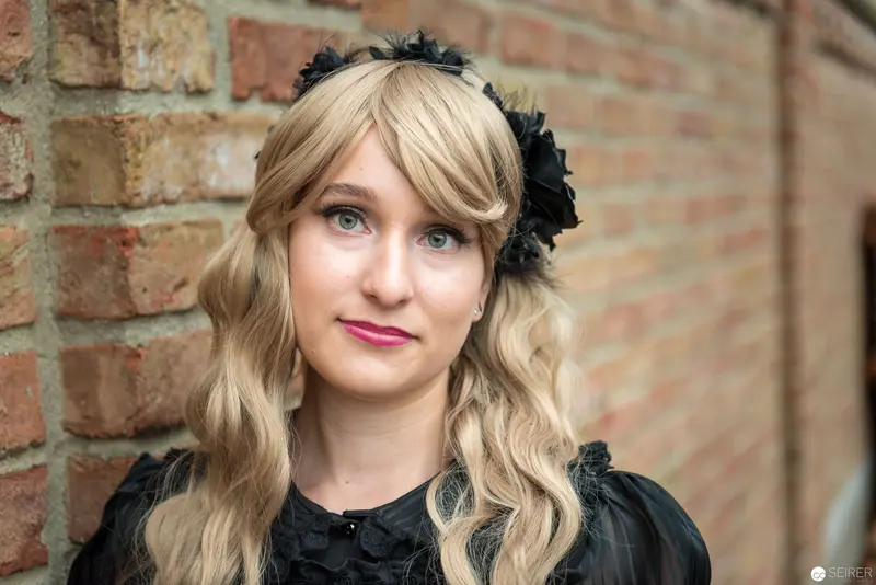 Blonde Woman in Black Attire Posing Against Brick Wall with Floral Headpiece