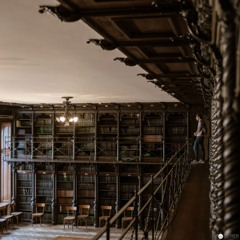 Multilevel Historical Library Interior with Ornate Shelving and Solitary Figure