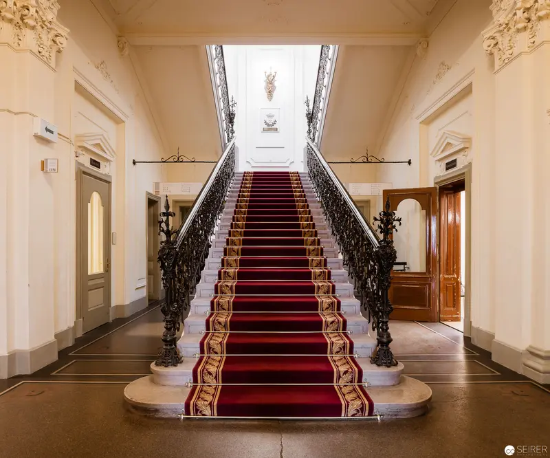 Grand Neoclassical Staircase with Ornate Red Carpet and Wrought-Iron Balustrade