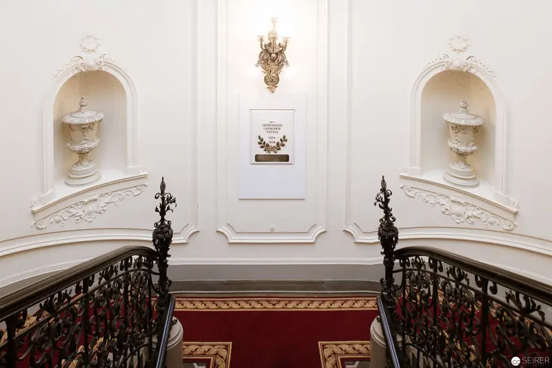 Neoclassical Staircase with Ornate Railings and White Sculptural Urns