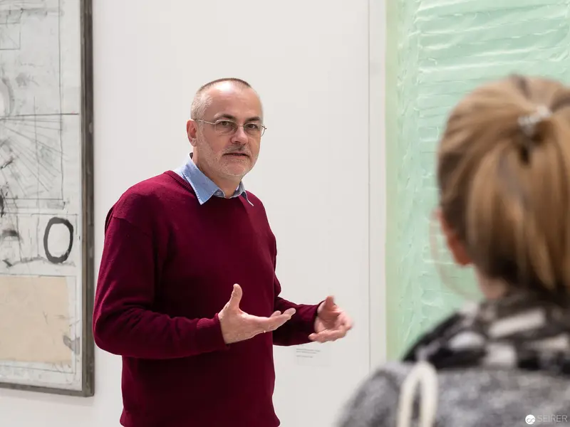 Curator in Burgundy Sweater Discusses Exhibition "Die 90er Jahre" at MUSA Vienna