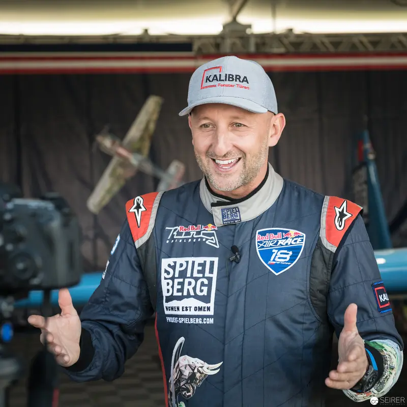 Red Bull Air Race Pilot in Racing Attire, Smiling in Workshop Setting