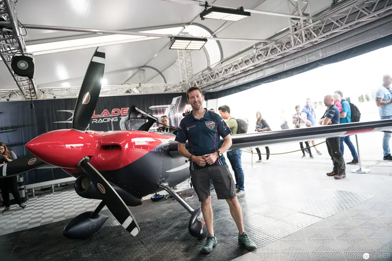 Red Bull Air Race Competitor Stands Beside Custom Racing Aircraft in Exhibition Space