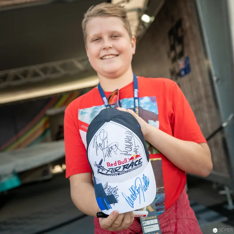 Red Bull Air Race Enthusiast Displays Signed Event Memorabilia with Joyful Expression