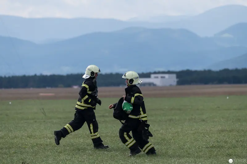 Firefighters Running Across Grassy Field with Mountain Landscape Behind